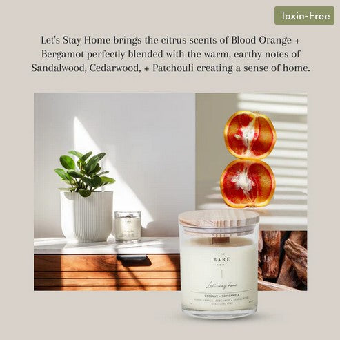 This 'Let's stay home' essential oil candle in a jar scented with blood orange, bergamot and sandalwood is shown beside a plant on a dresser and also in front of a slice blood orange and some sandalwood.