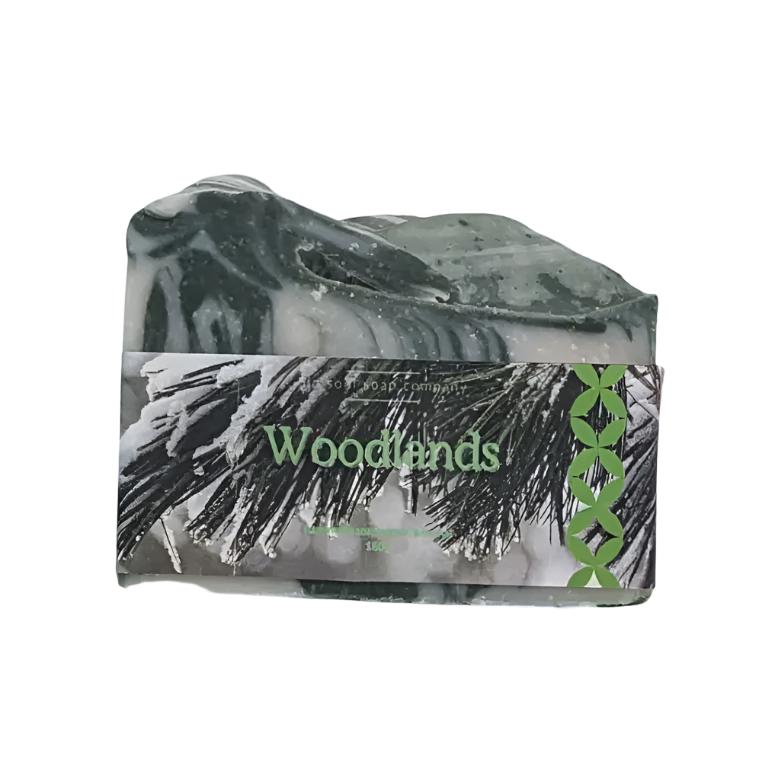 A warm woodsy fragrant handcrafted artisan top bar soap with word 'Woodlands' on a photo label showing snow on a pine tree. The soap is on a white background 