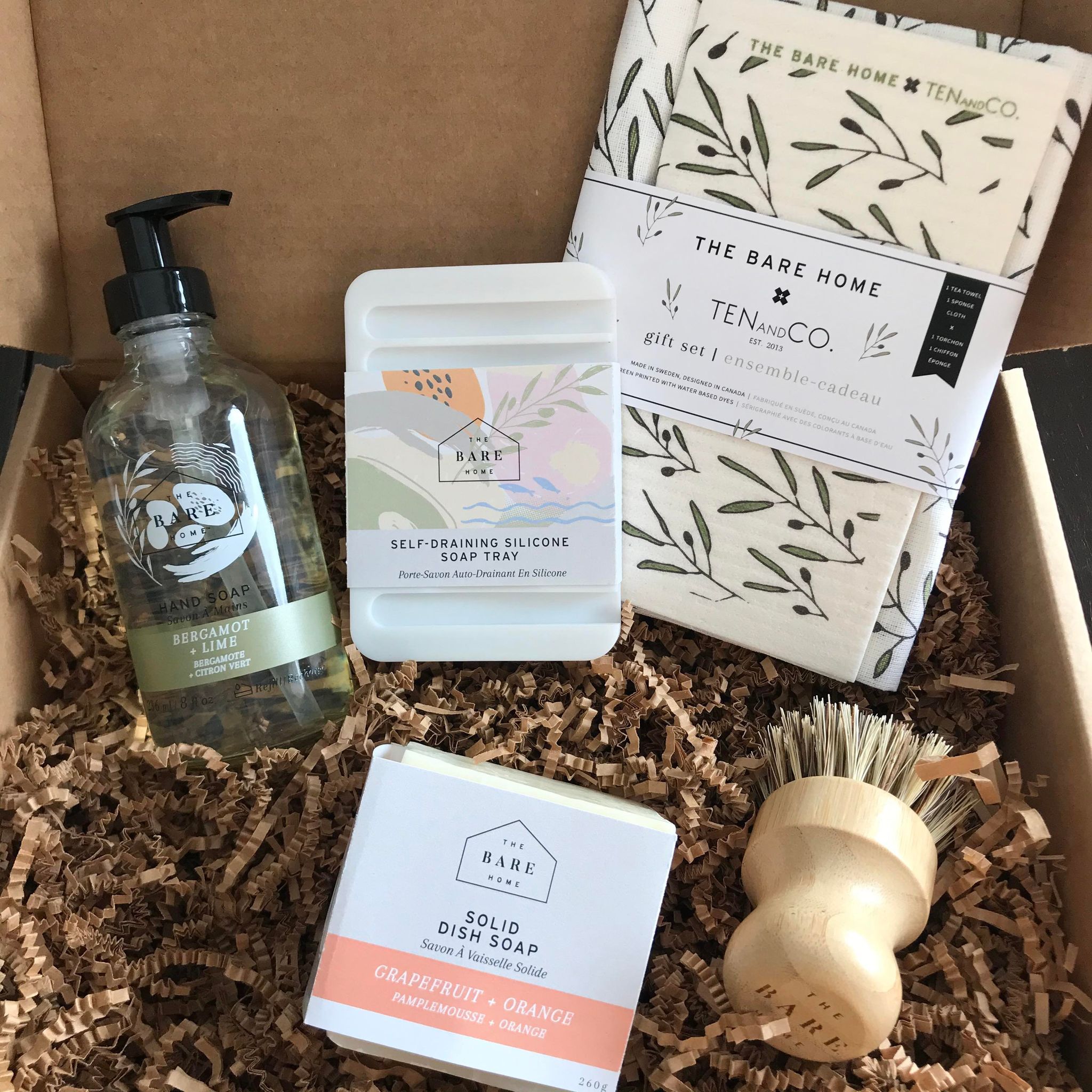This bergamot lime kitchen scrubber gift set features a olive TEN and CO. sponge cloth and tea towel set, a refillable 236 ml bergamot lime hand soap in glass bottle, a white silicone soap dish, a grapefruit and orange dish soap bar and either a pot scrubber brush and comes in a brown kraft box