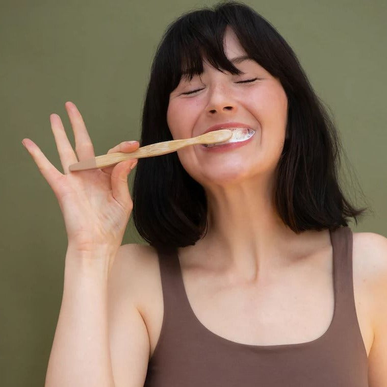 Woman brushing her teeth with a bamboo toothbrush a fresh mint Canadian made Tanit toothpaste tablet