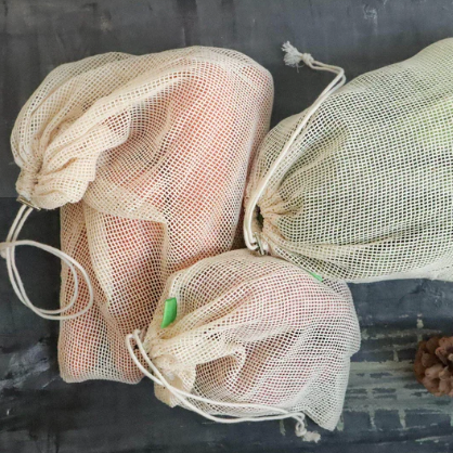 Set of three organic cotton mesh produce bags with drawstrings filled with fresh carrots, sweet potatoes and lettuce