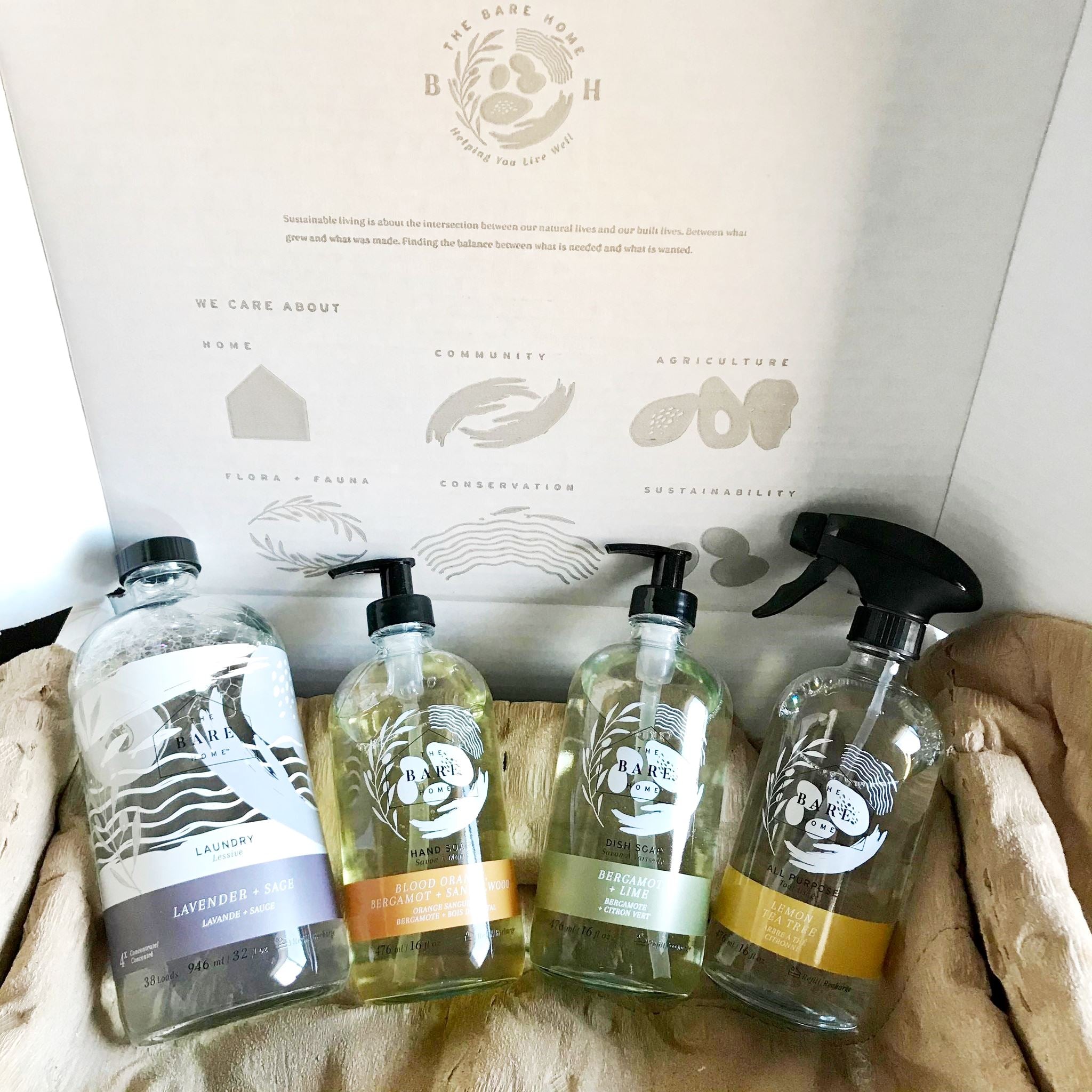 Liquid essential oil scented laundry detergent, hand soap, dish soap and all purpose cleaner in refillable glass bottles packaged together in a box as a way to sample the line of eco sustainable household products made in Canada by The Bare Home company based in Ontario
