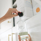 a bergamot lime glass refill bottle being refilled from 3 L refill box sitting in a cupboardf