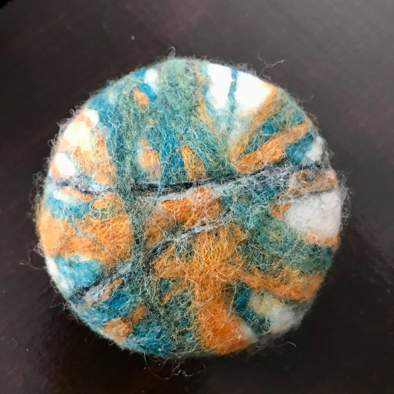 round natural essential oil craft beer felted soap with a citrus ginger scent and hand felted with 100 percent wook in shades of green with orange, black and white highlights
