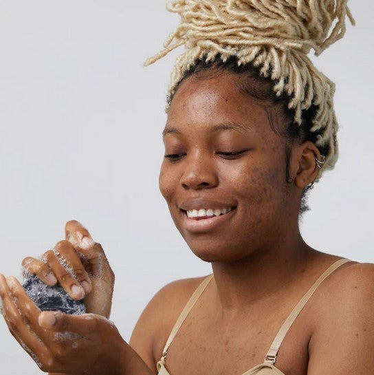 Woman lathering up a bar of round facial cleansing soap with activated charcoal soap made in Canada by Birch Baben