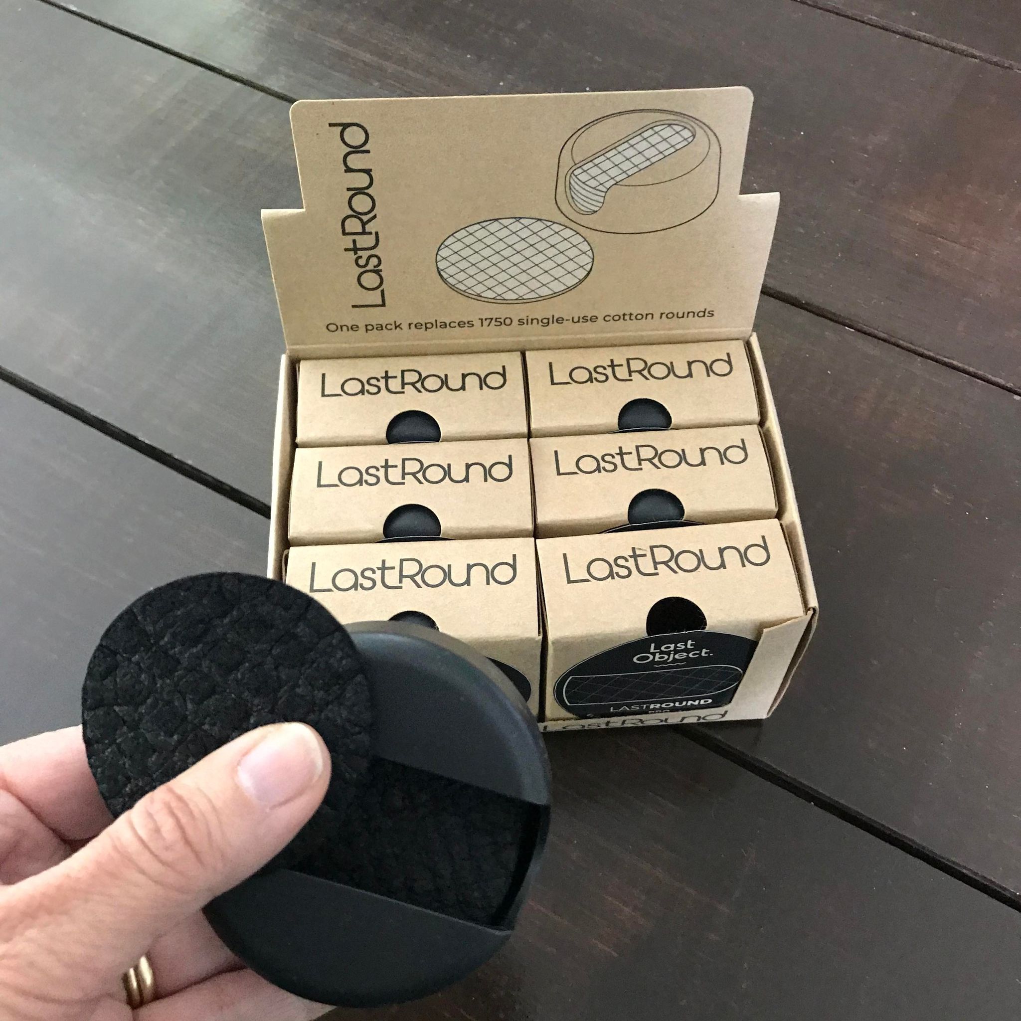LastRound black regular size reusable cotton rounds in a black case held in front of a display case of the same reusable makeup remover pads in boxes