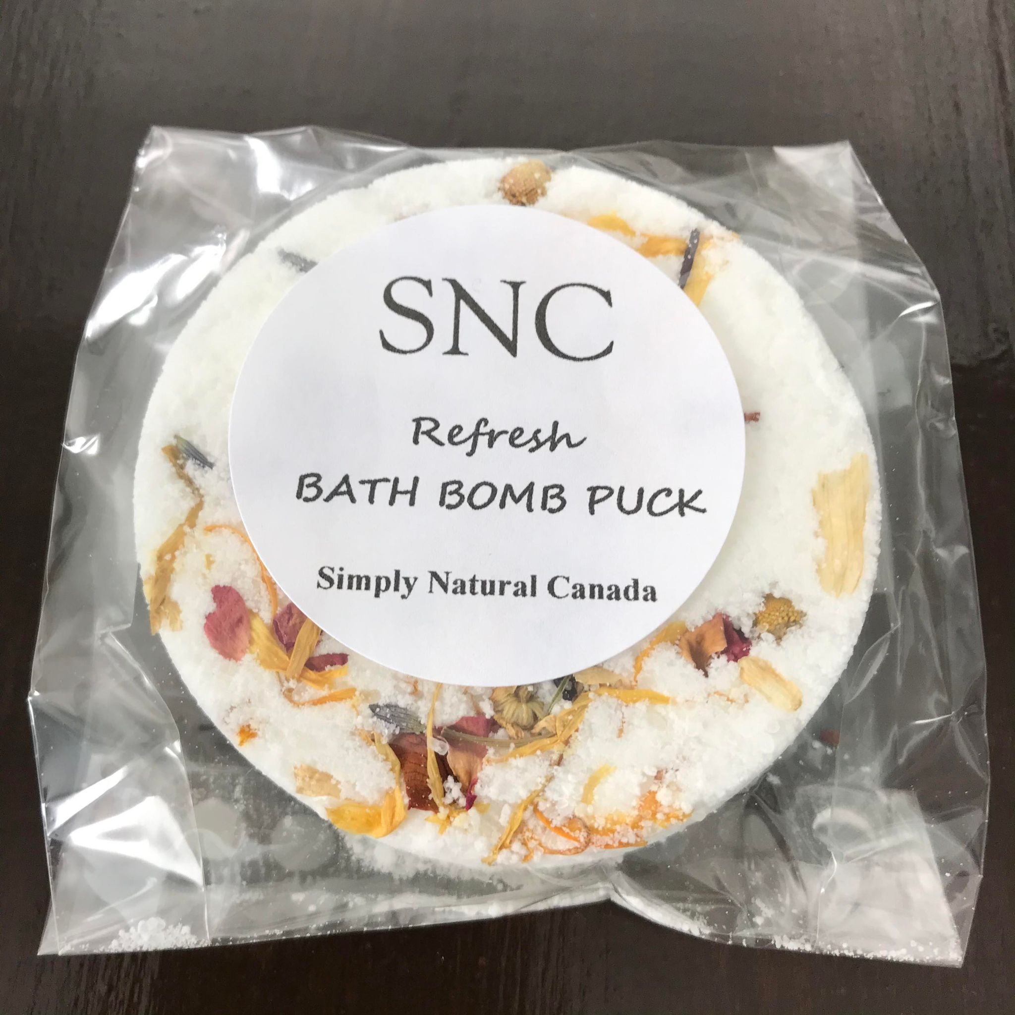 canadian made refresh bath bomb puck features dried flowers and a crisp fresh essential oil blend and comes in clear compostable wrap
