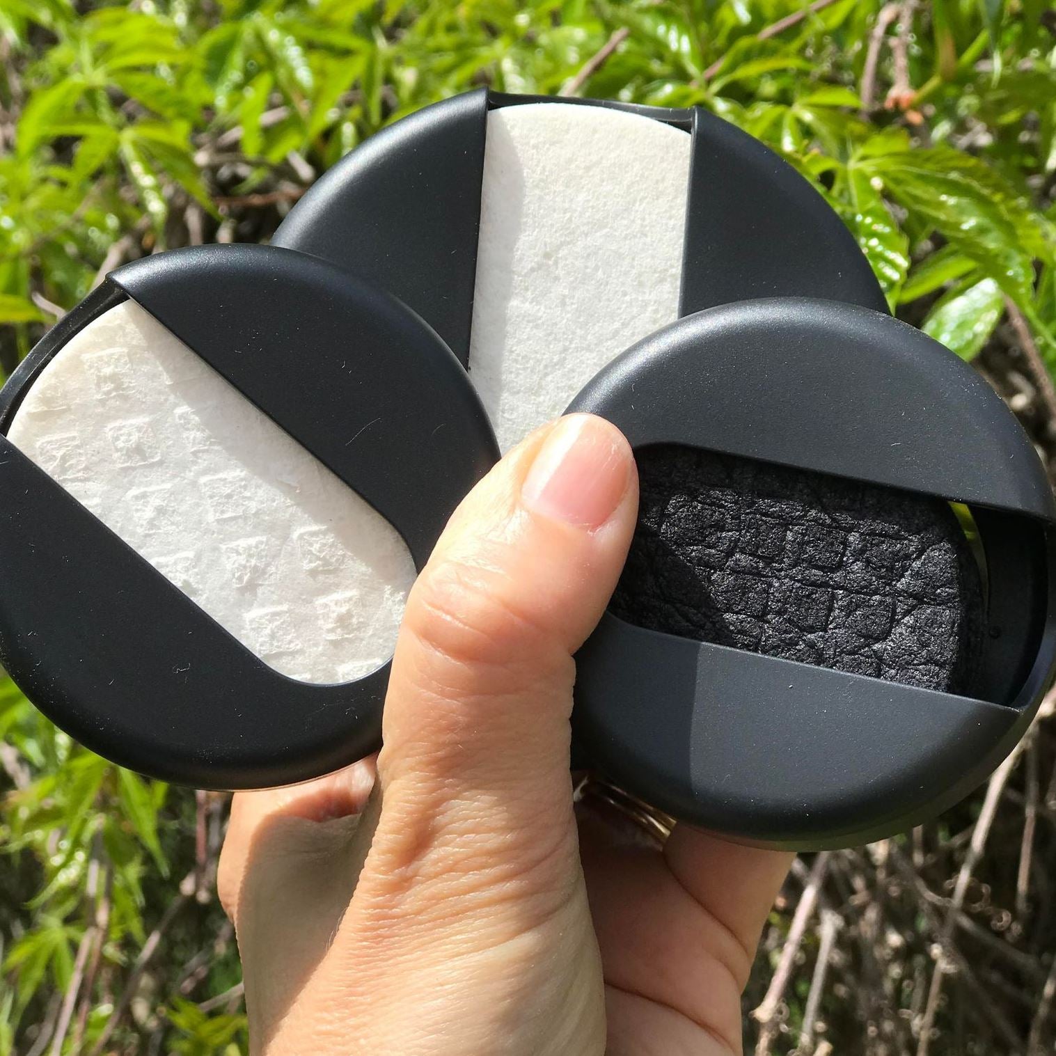 A hand holding Last Object reusable and compostable LastRound makeup remover pads in black and white regular size and large white rounds in a black case made with recycled ocean plastics