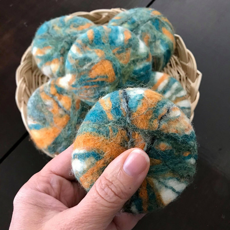 hand felted oval citrus beer soap made in canada and felted in shades of green with orange and black highlights on a white wool background